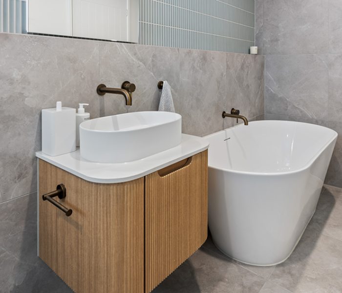 A modern bathroom with large tiles, timber vanity with a freestanding curved tub