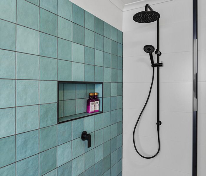 A modern bathroom with turquoise textured tiles and black tapware and fixtures